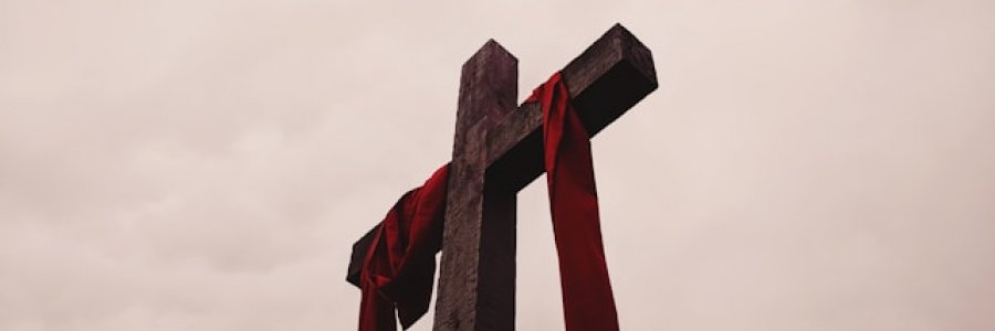 Image shows a low angle view of a cross with a red garment draped over the cross piece.