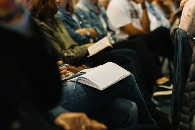 Image shows people sitting on chairs taking notes during a church service.